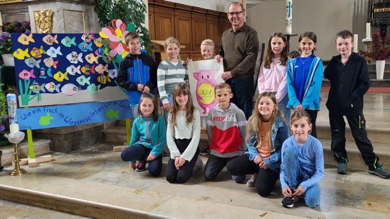 Kinder knien und stehen vor dem Altar in der Kirche und zeigen mit dem Geschäftsführer des Club 82 ein Plakat mit der Spendensumme